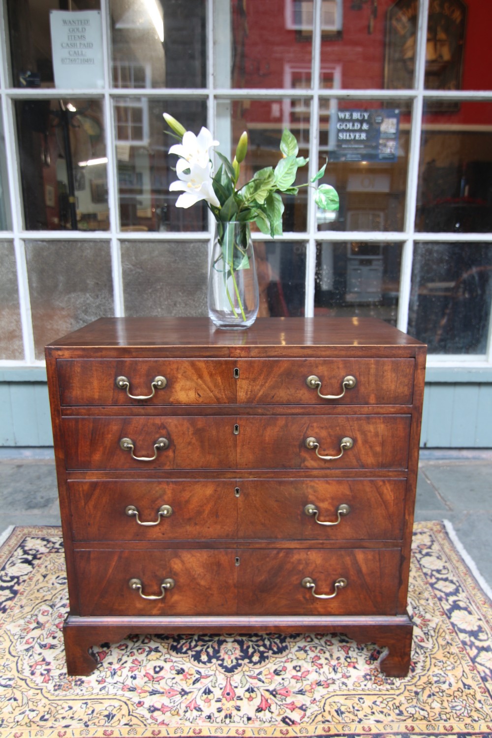 A late Georgian mahogany chest of four full-width drawers featuring flame mahogany veneer fronts, brass swan-neck handles, keyhole escutcheons, and bracket feet.