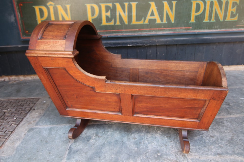 A late Georgian mahogany rocking crib featuring an integrated curved wooden hood, recessed side panels, and shaped rocker feet.