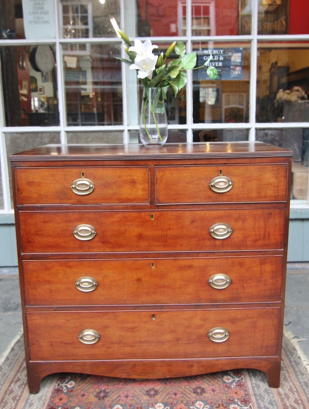 A Regency mahogany chest of drawers featuring two short drawers above three long graduated drawers with brass oval handles and a shaped apron.