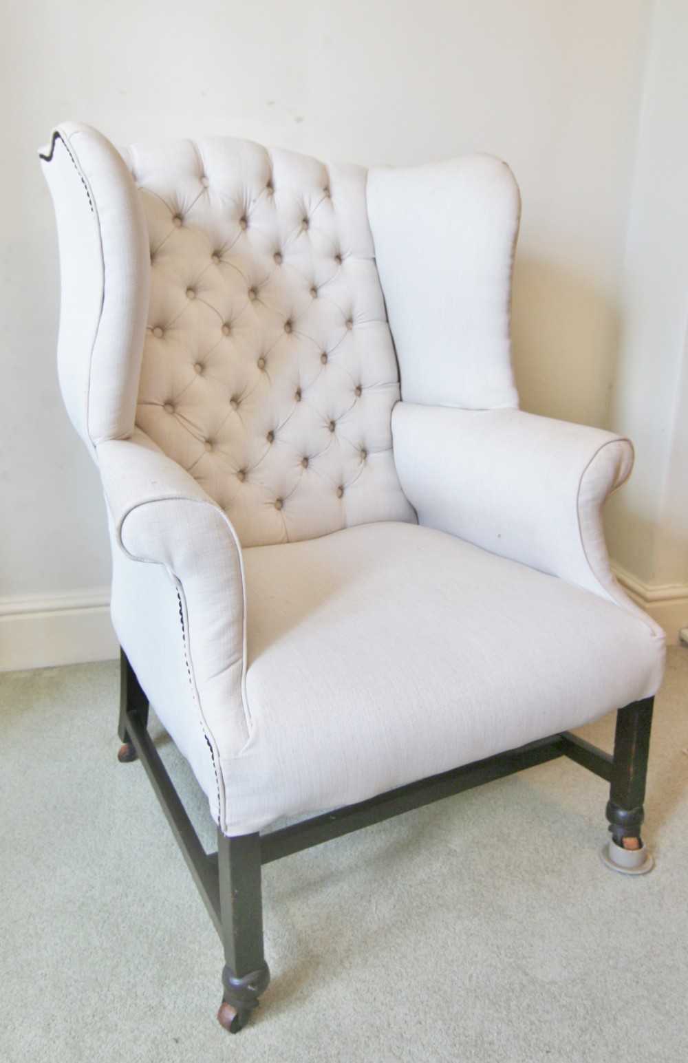 An eighteenth-century Mid-Georgian wing armchair upholstered in off-white fabric with deep buttoning on the backrest and dark mahogany legs with castors.
