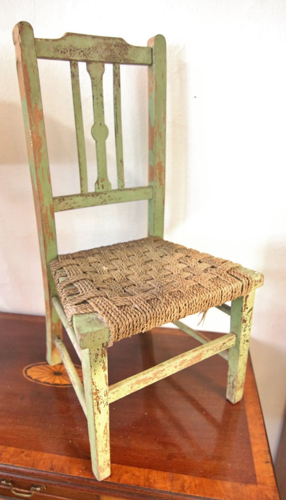 A 19th-century Welsh childs chair featuring distressed pale green paint, vertical back splats, and a woven rush seat.