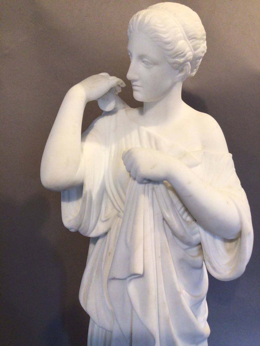 A 19th-century carved white marble statue of a classical figure wearing draped robes, standing on a rectangular integral base. View XIV