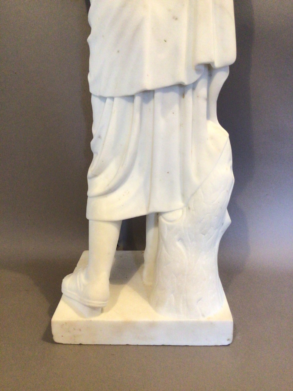 A 19th-century carved white marble statue of a classical figure wearing draped robes, standing on a rectangular integral base. View XX