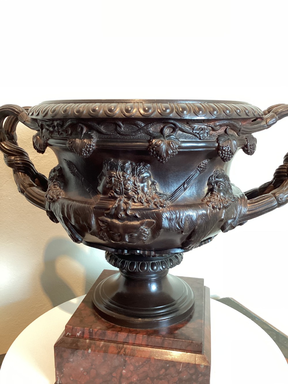 A dark patinated bronze Warwick vase with entwined vine handles and classical relief masks, set atop a square red marble plinth. View IX
