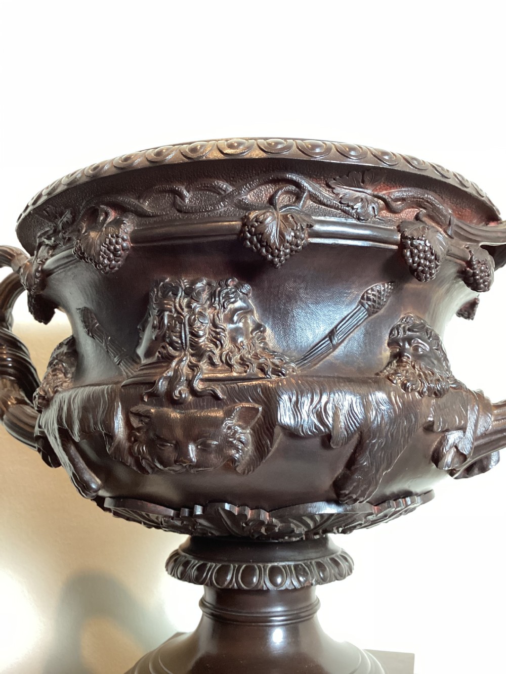 A dark patinated bronze Warwick vase with entwined vine handles and classical relief masks, set atop a square red marble plinth. View X