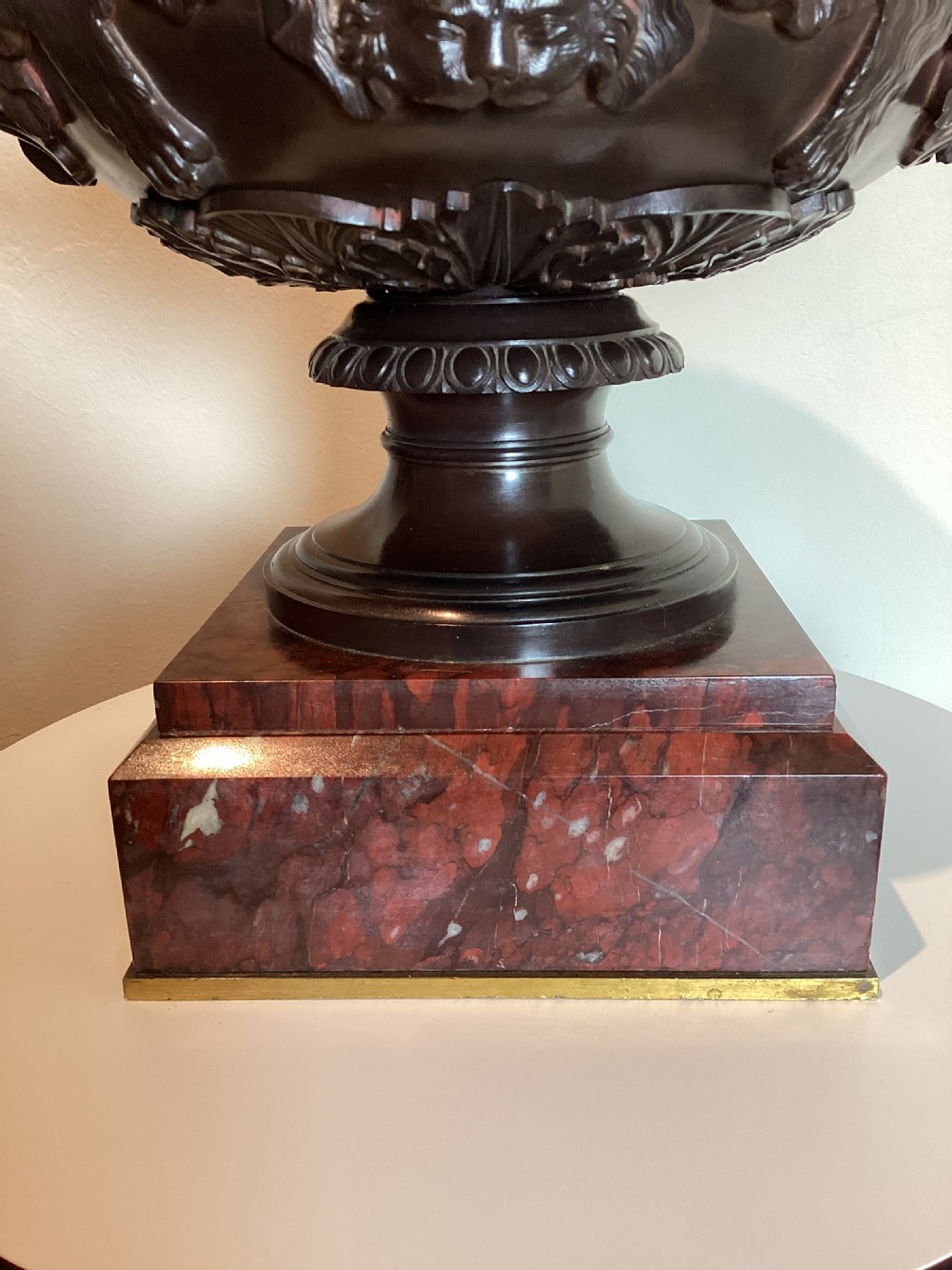 A dark patinated bronze Warwick vase with entwined vine handles and classical relief masks, set atop a square red marble plinth. View XVI