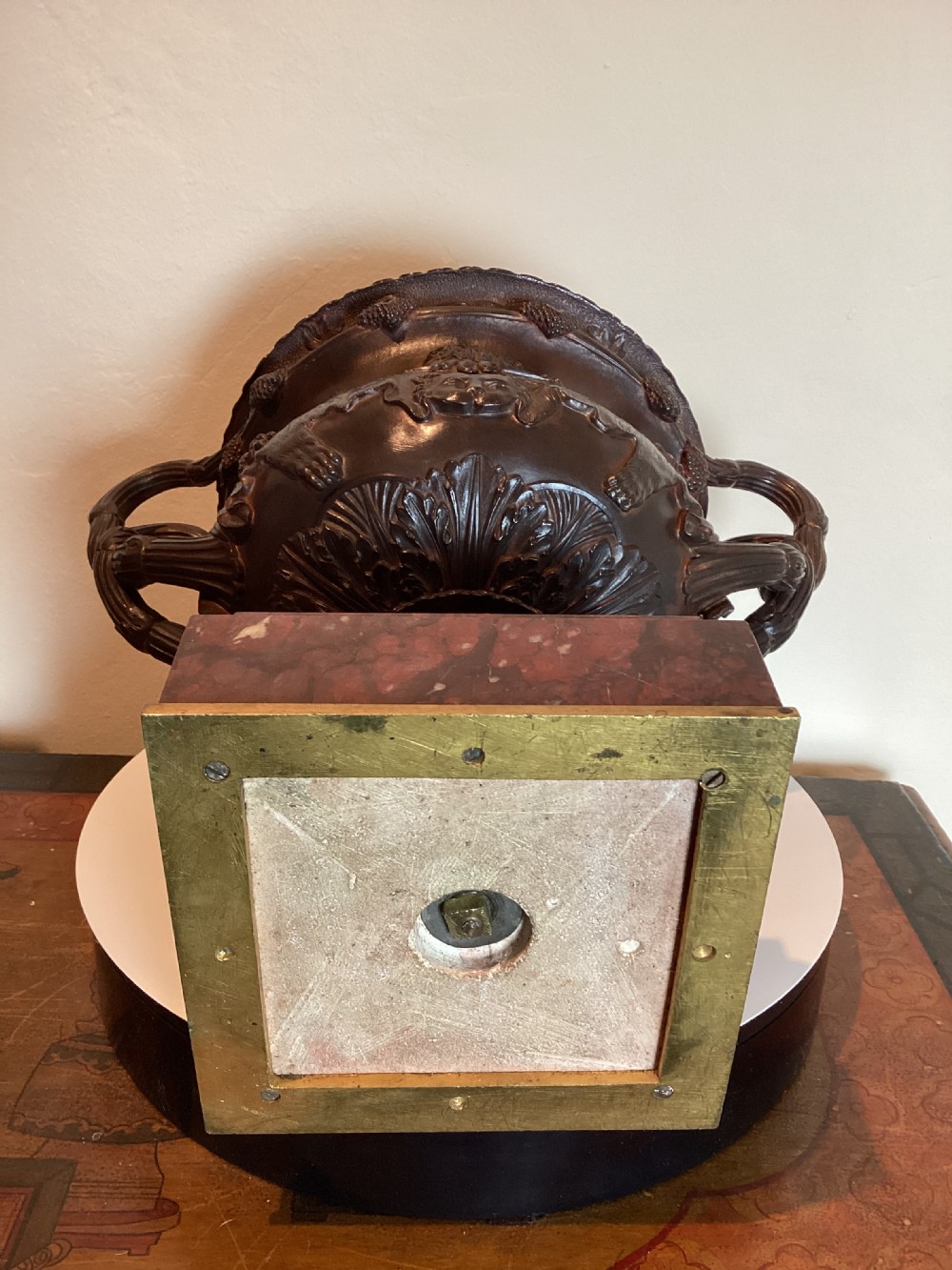 A dark patinated bronze Warwick vase with entwined vine handles and classical relief masks, set atop a square red marble plinth. View XVII