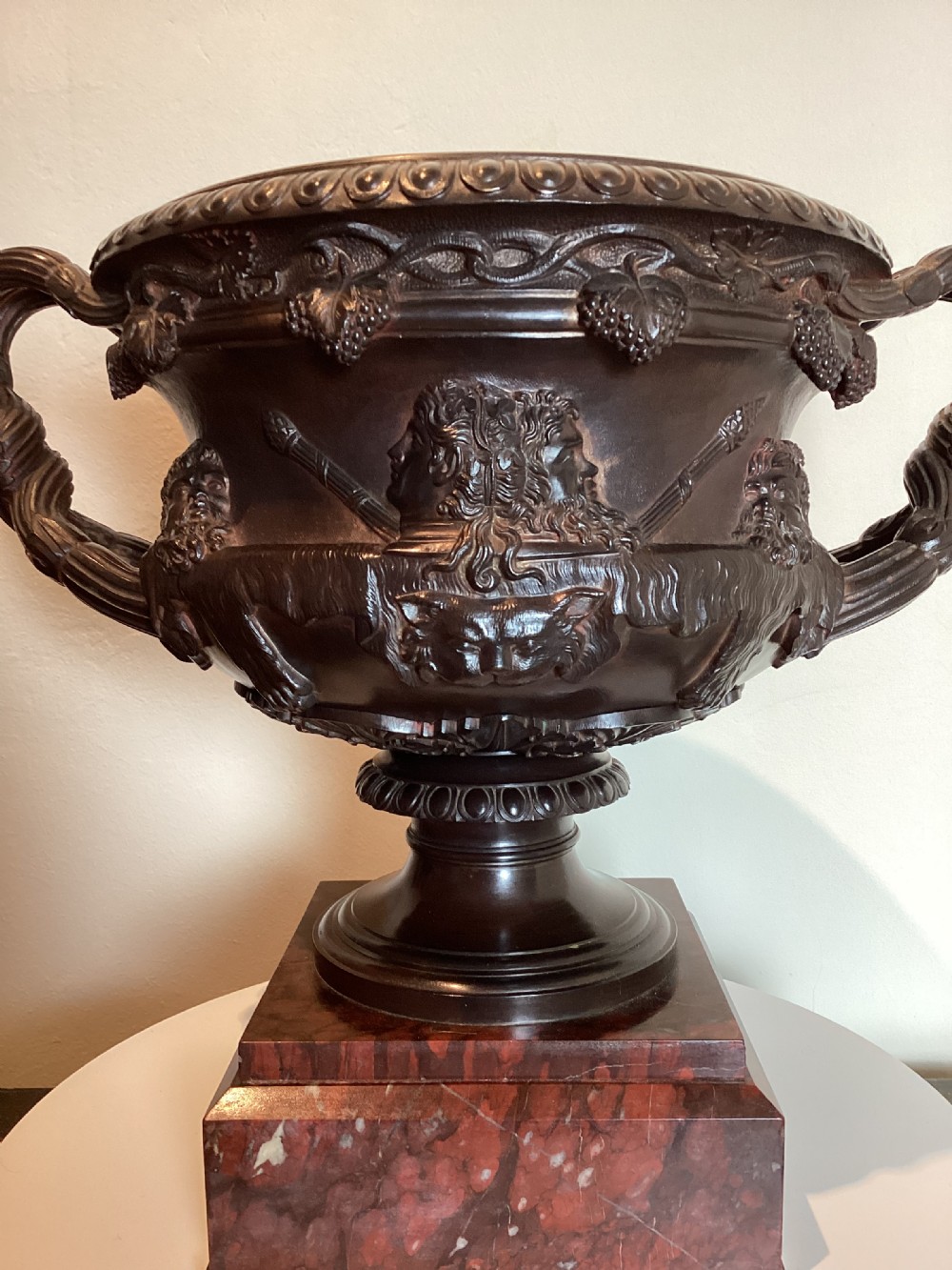 A dark patinated bronze Warwick vase with entwined vine handles and classical relief masks, set atop a square red marble plinth. View XVIII