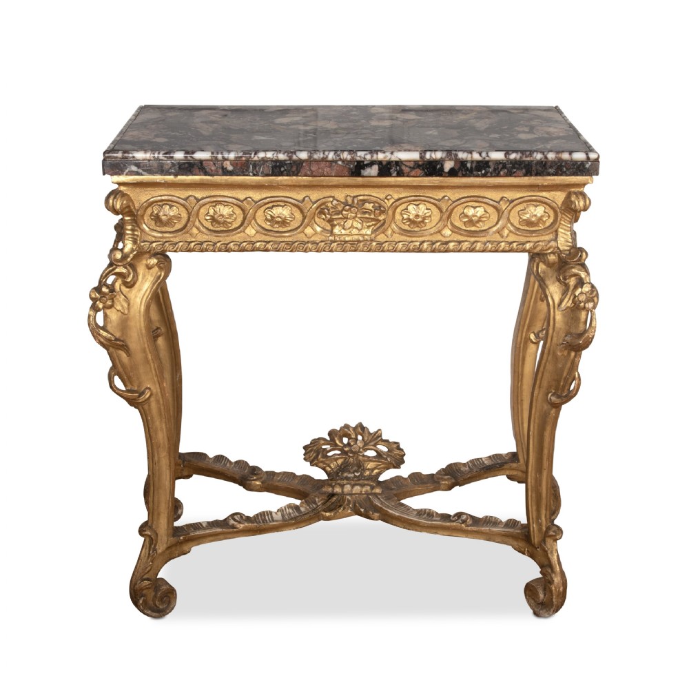 An 18th-century giltwood console table featuring a dark mottled marble top, carved apron with rosette motifs, and cabriole legs linked by an X-shaped stretcher.
