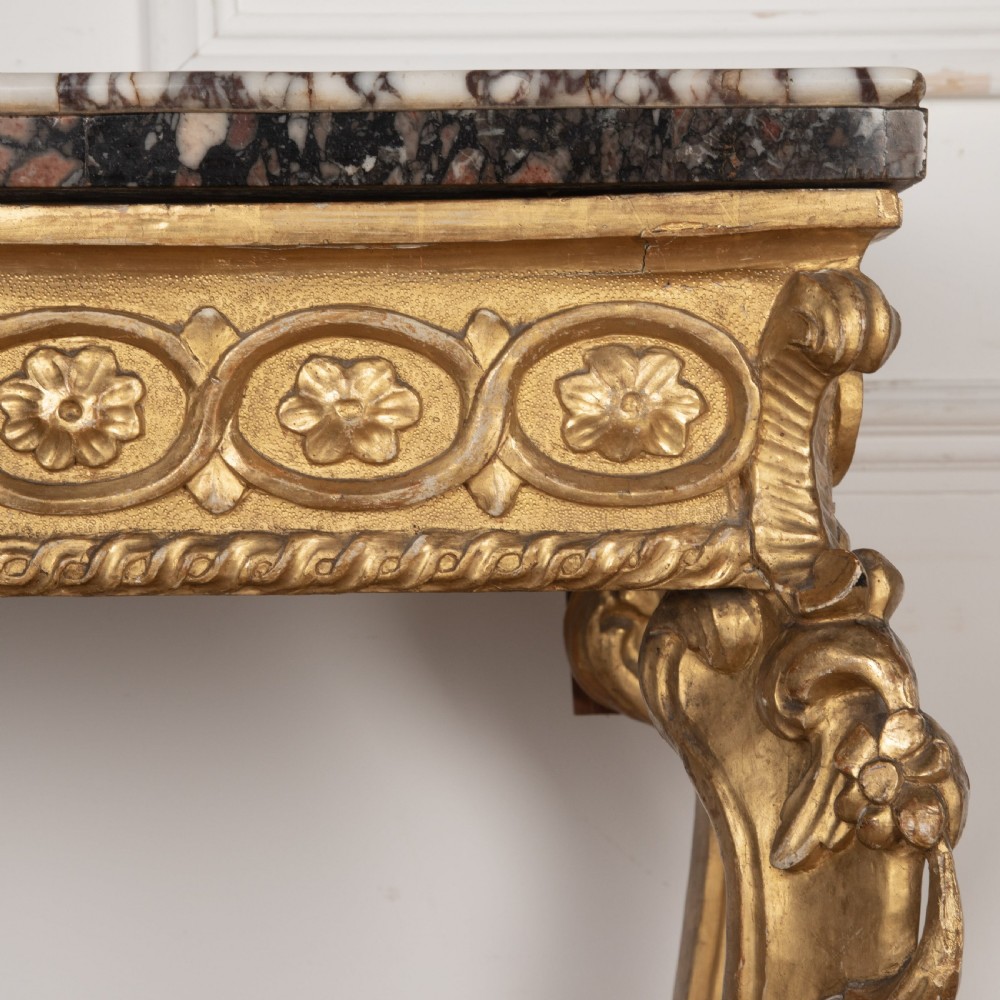 An 18th-century giltwood console table featuring a dark mottled marble top, carved apron with rosette motifs, and cabriole legs linked by an X-shaped stretcher. View VI