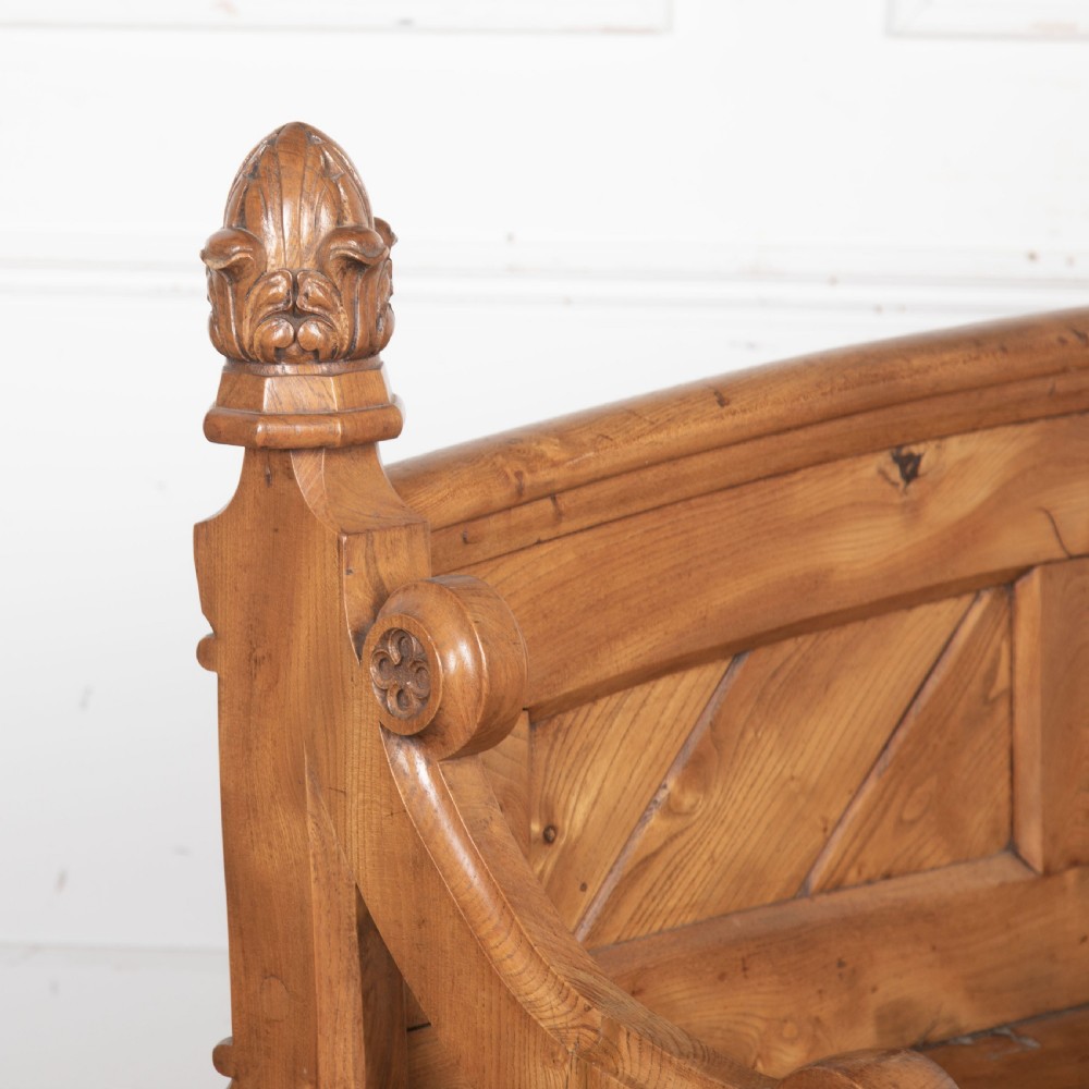 A 19th-century carved elm bench featuring pointed finial posts, a geometric panelled backrest, and trefoil cut-outs on the lower frame. View III
