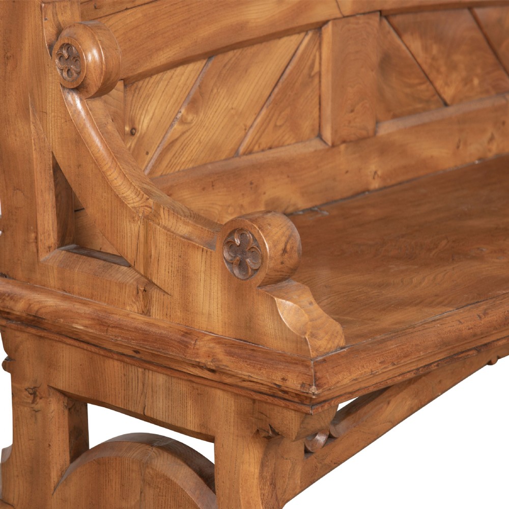 A 19th-century carved elm bench featuring pointed finial posts, a geometric panelled backrest, and trefoil cut-outs on the lower frame. View IV