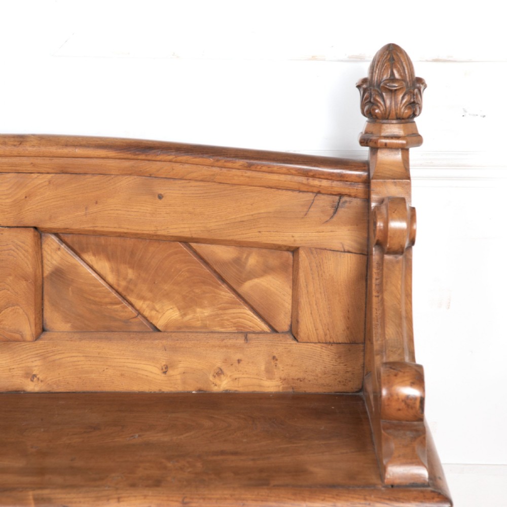 A 19th-century carved elm bench featuring pointed finial posts, a geometric panelled backrest, and trefoil cut-outs on the lower frame. View VI