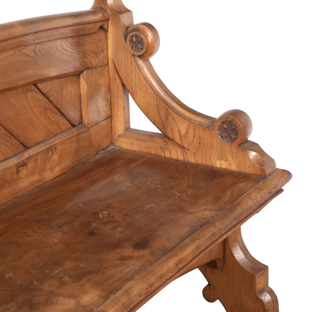 A 19th-century carved elm bench featuring pointed finial posts, a geometric panelled backrest, and trefoil cut-outs on the lower frame. View VIII