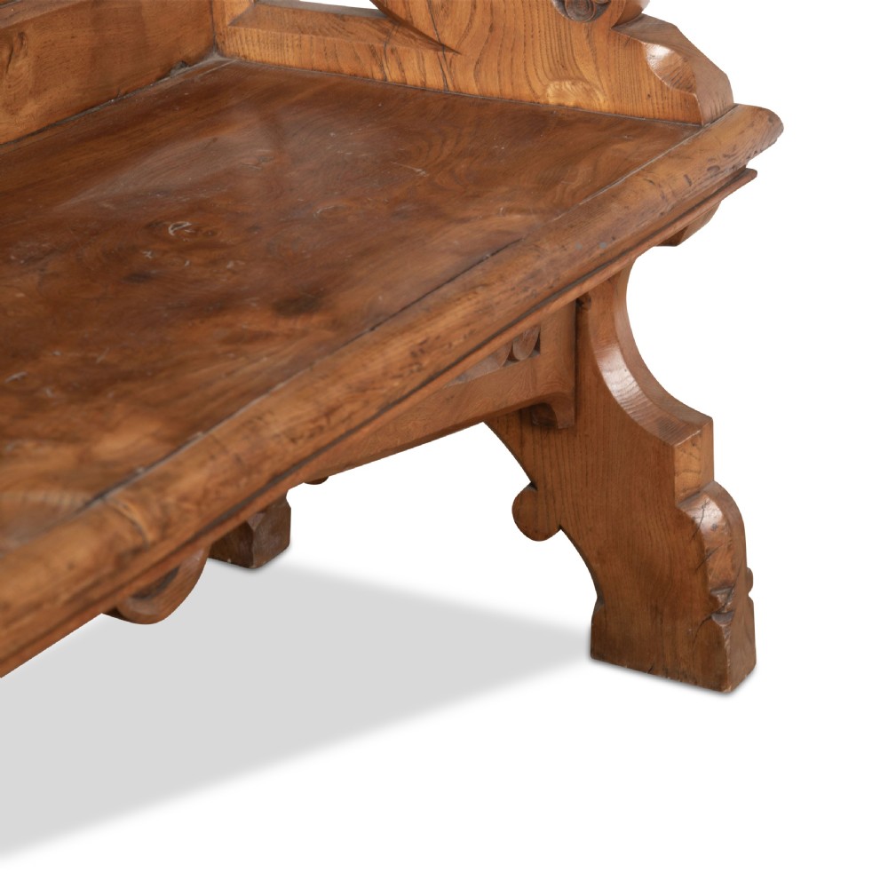 A 19th-century carved elm bench featuring pointed finial posts, a geometric panelled backrest, and trefoil cut-outs on the lower frame. View IX