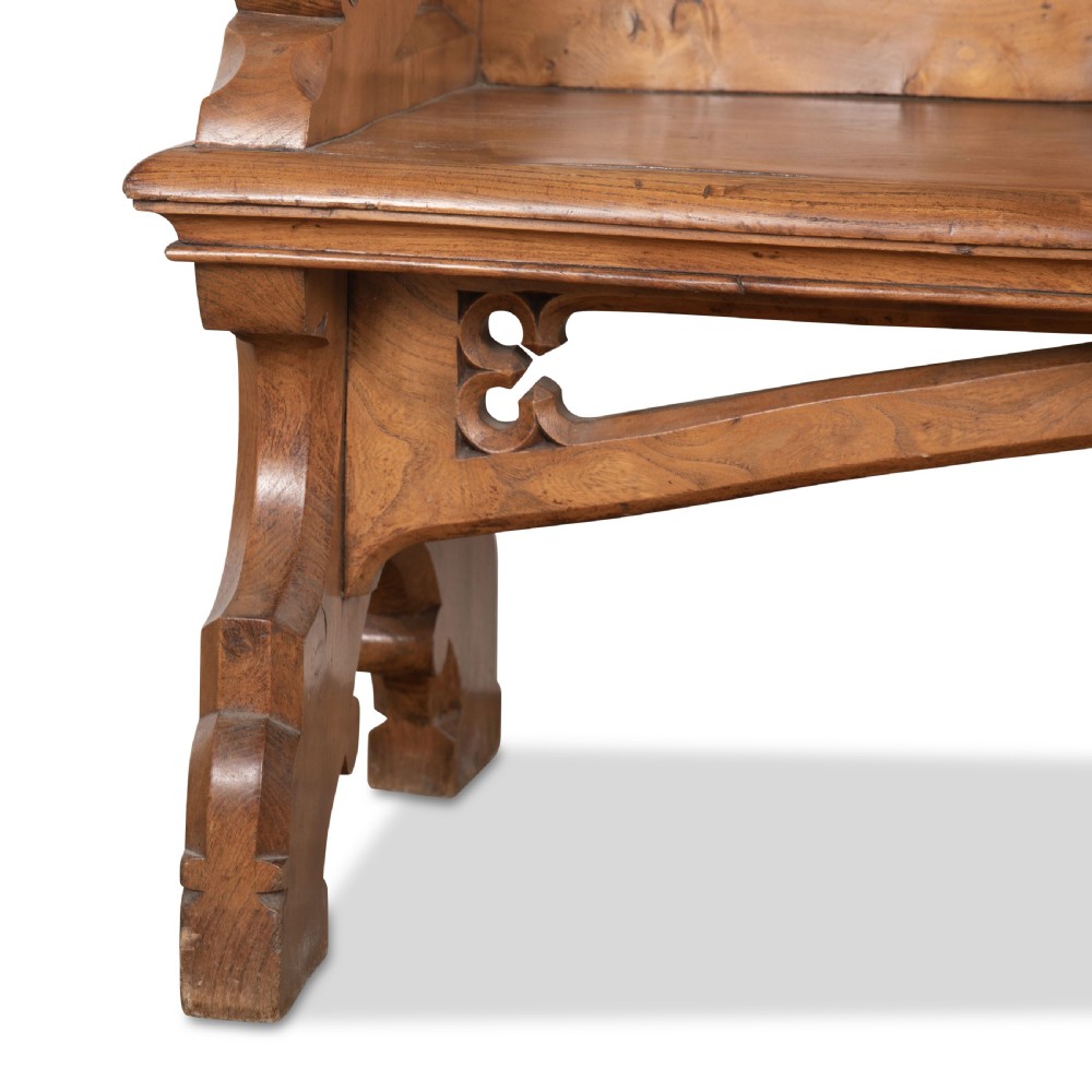 A 19th-century carved elm bench featuring pointed finial posts, a geometric panelled backrest, and trefoil cut-outs on the lower frame. View XI
