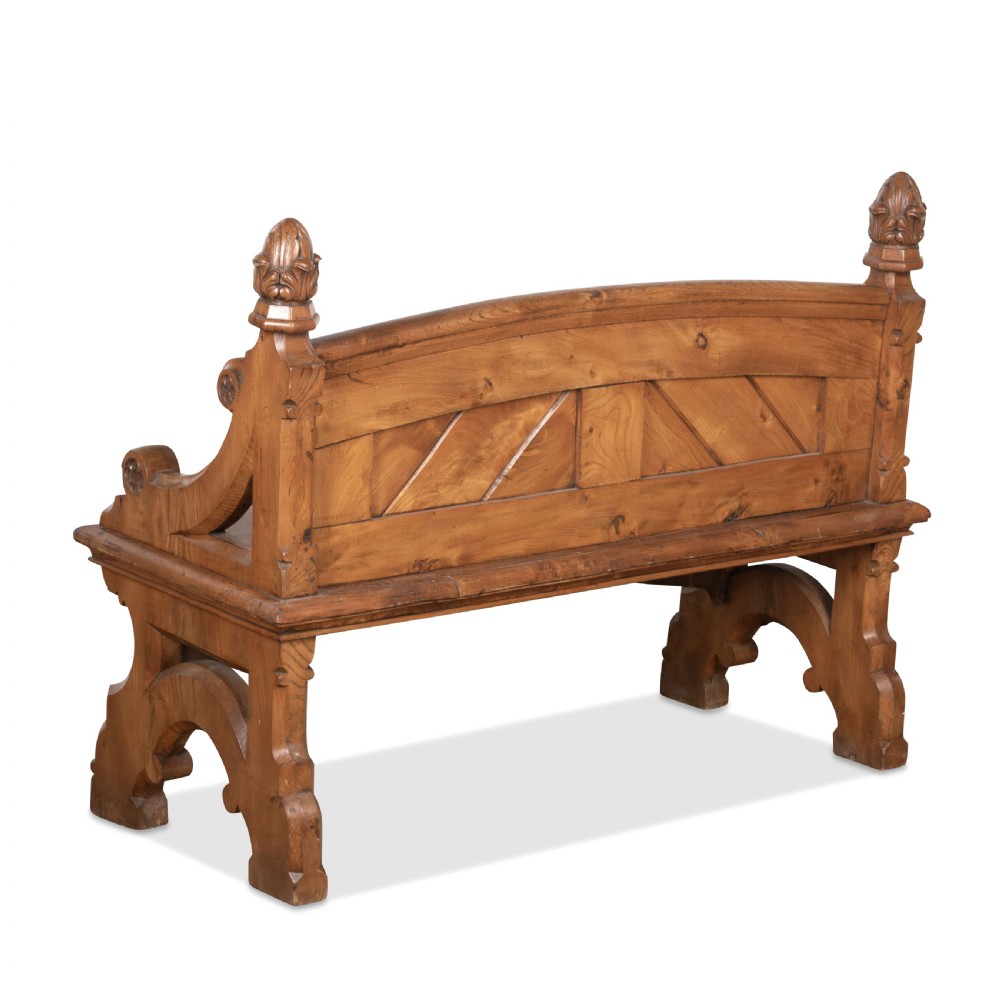 A 19th-century carved elm bench featuring pointed finial posts, a geometric panelled backrest, and trefoil cut-outs on the lower frame. View XV