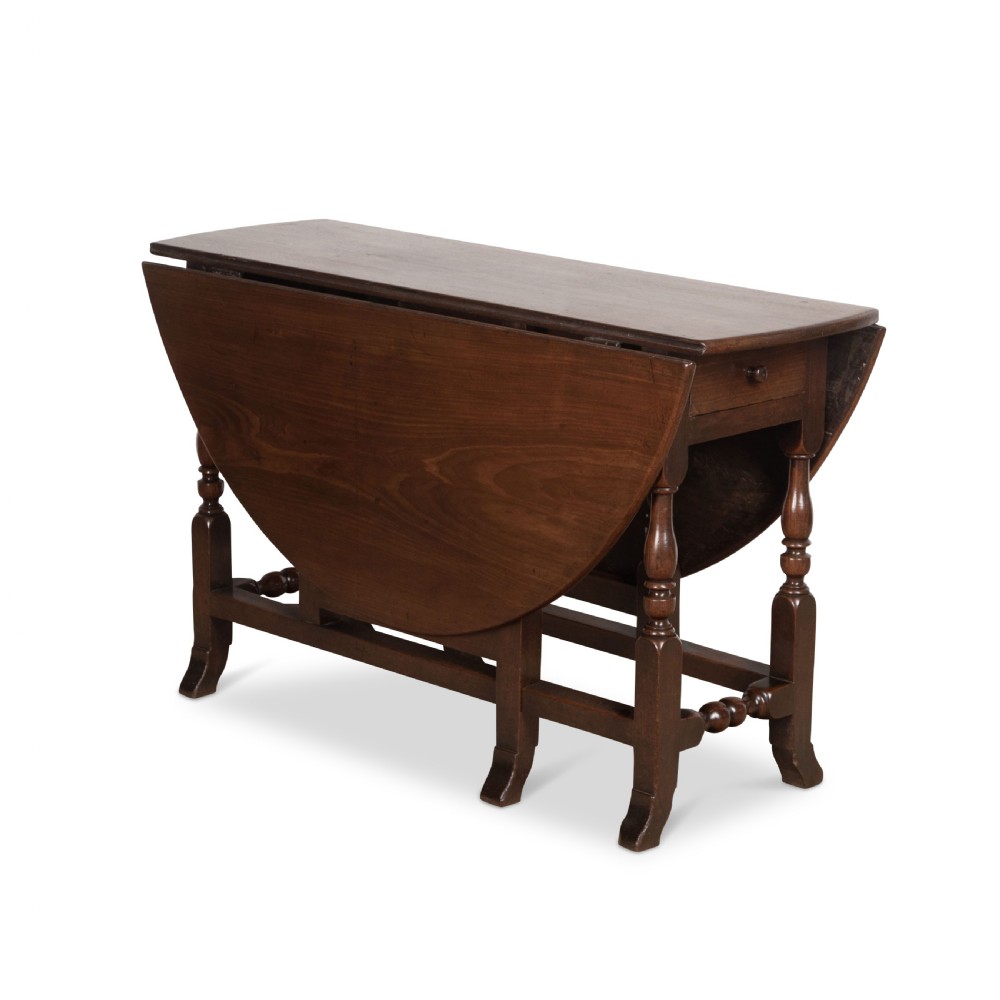 A dark brown Georgian walnut drop flap dining table featuring turned legs, bottom stretchers, an end drawer, and hinged oval leaves.