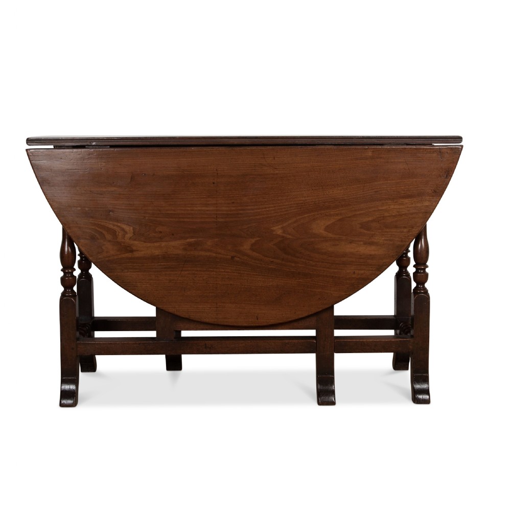 A dark brown Georgian walnut drop flap dining table featuring turned legs, bottom stretchers, an end drawer, and hinged oval leaves. View III