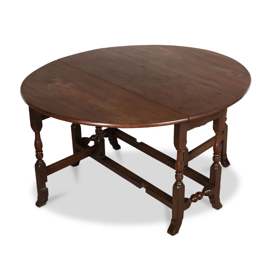 A dark brown Georgian walnut drop flap dining table featuring turned legs, bottom stretchers, an end drawer, and hinged oval leaves. View VII