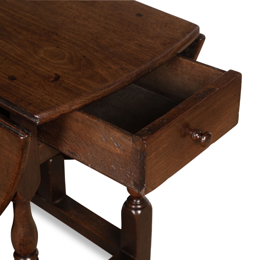 A dark brown Georgian walnut drop flap dining table featuring turned legs, bottom stretchers, an end drawer, and hinged oval leaves. View IX