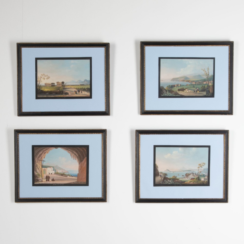 A set of four framed 19th-century Neapolitan gouache landscape paintings depicting coastal scenes and classical Italian ruins in dark wooden frames with light blue mounts.