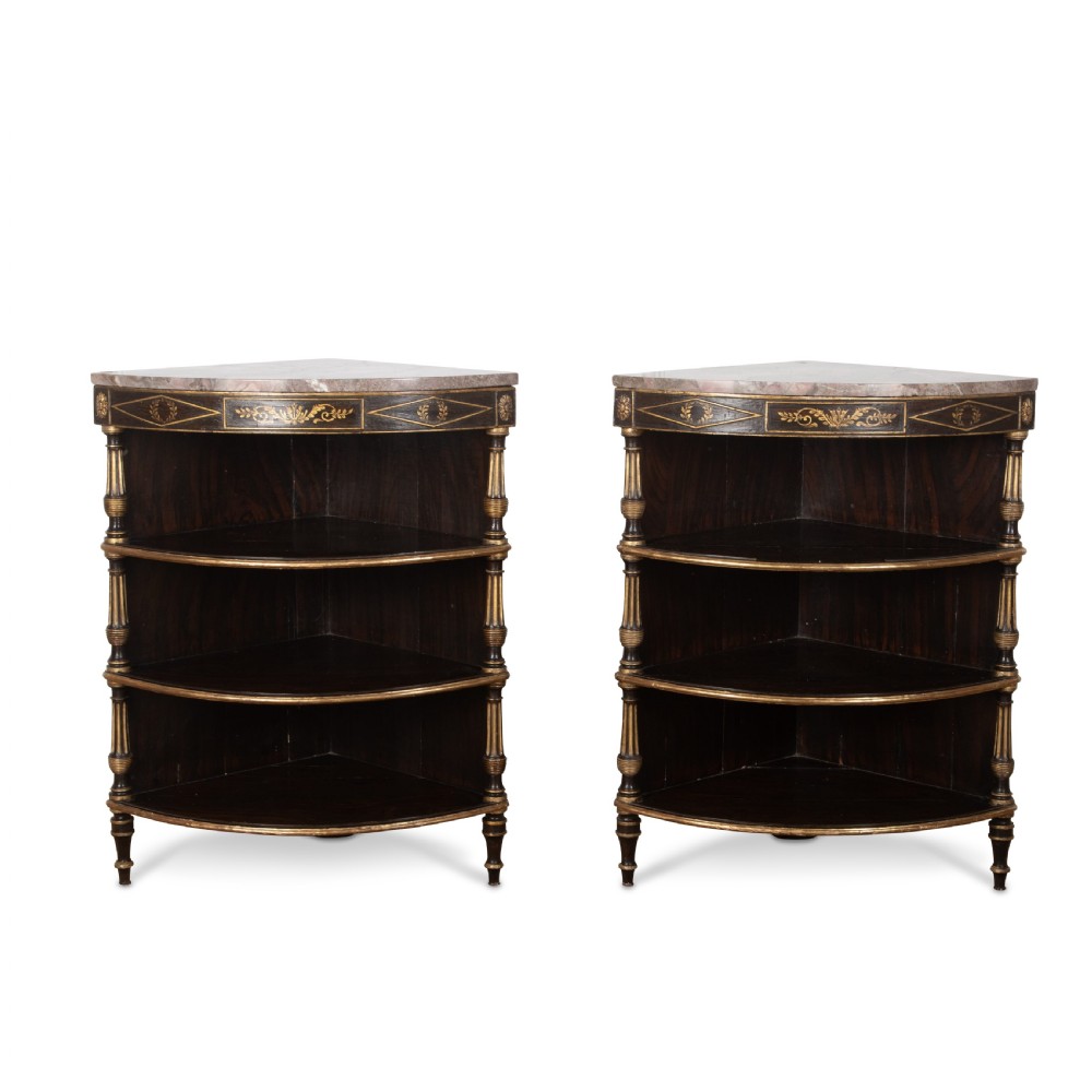 A pair of Regency-style black painted open corner cabinets featuring marble tops, gilt floral scrollwork friezes, and turned support columns.