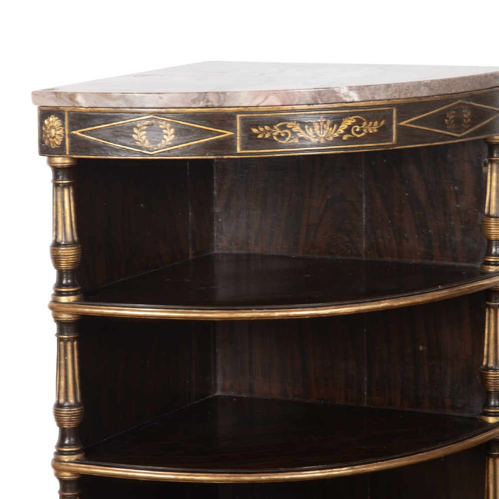A pair of Regency-style black painted open corner cabinets featuring marble tops, gilt floral scrollwork friezes, and turned support columns. View V