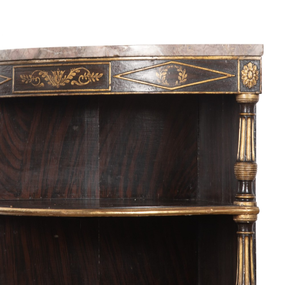A pair of Regency-style black painted open corner cabinets featuring marble tops, gilt floral scrollwork friezes, and turned support columns. View IX