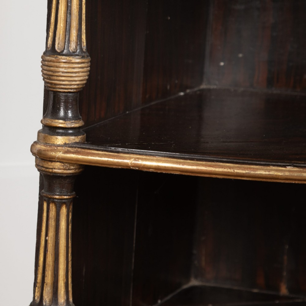 A pair of Regency-style black painted open corner cabinets featuring marble tops, gilt floral scrollwork friezes, and turned support columns. View X