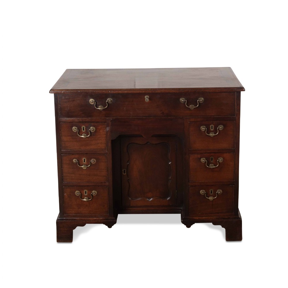 An 18th-century dark mahogany kneehole desk featuring a long top drawer above six side drawers and a central recessed cupboard door with brass handles.