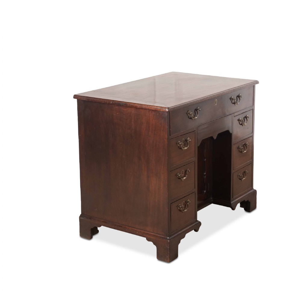 An 18th-century dark mahogany kneehole desk featuring a long top drawer above six side drawers and a central recessed cupboard door with brass handles. View V