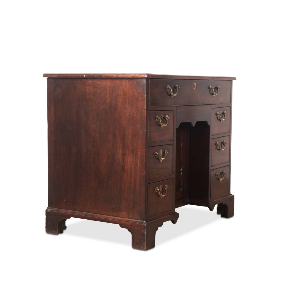 An 18th-century dark mahogany kneehole desk featuring a long top drawer above six side drawers and a central recessed cupboard door with brass handles. View VI