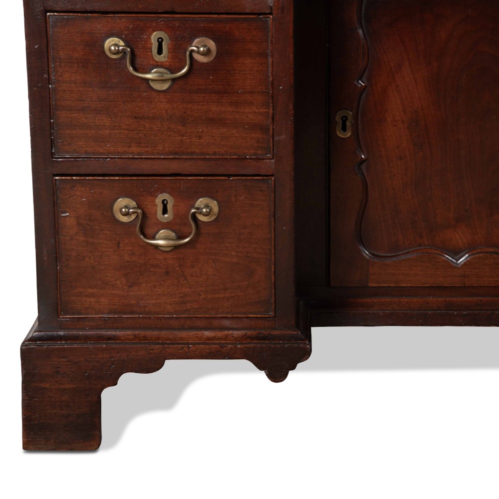 An 18th-century dark mahogany kneehole desk featuring a long top drawer above six side drawers and a central recessed cupboard door with brass handles. View VIII