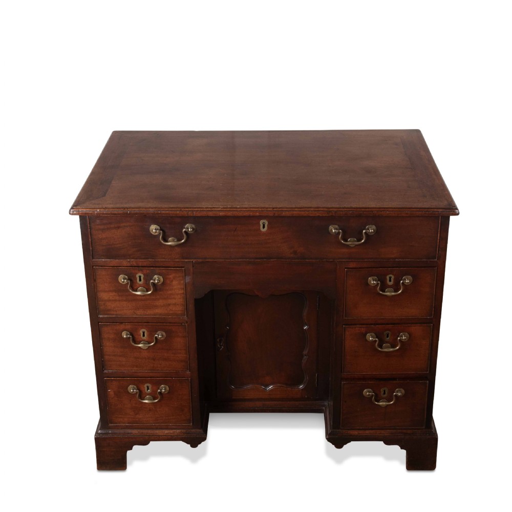 An 18th-century dark mahogany kneehole desk featuring a long top drawer above six side drawers and a central recessed cupboard door with brass handles. View X
