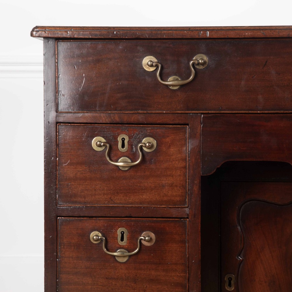 An 18th-century dark mahogany kneehole desk featuring a long top drawer above six side drawers and a central recessed cupboard door with brass handles. View XIII