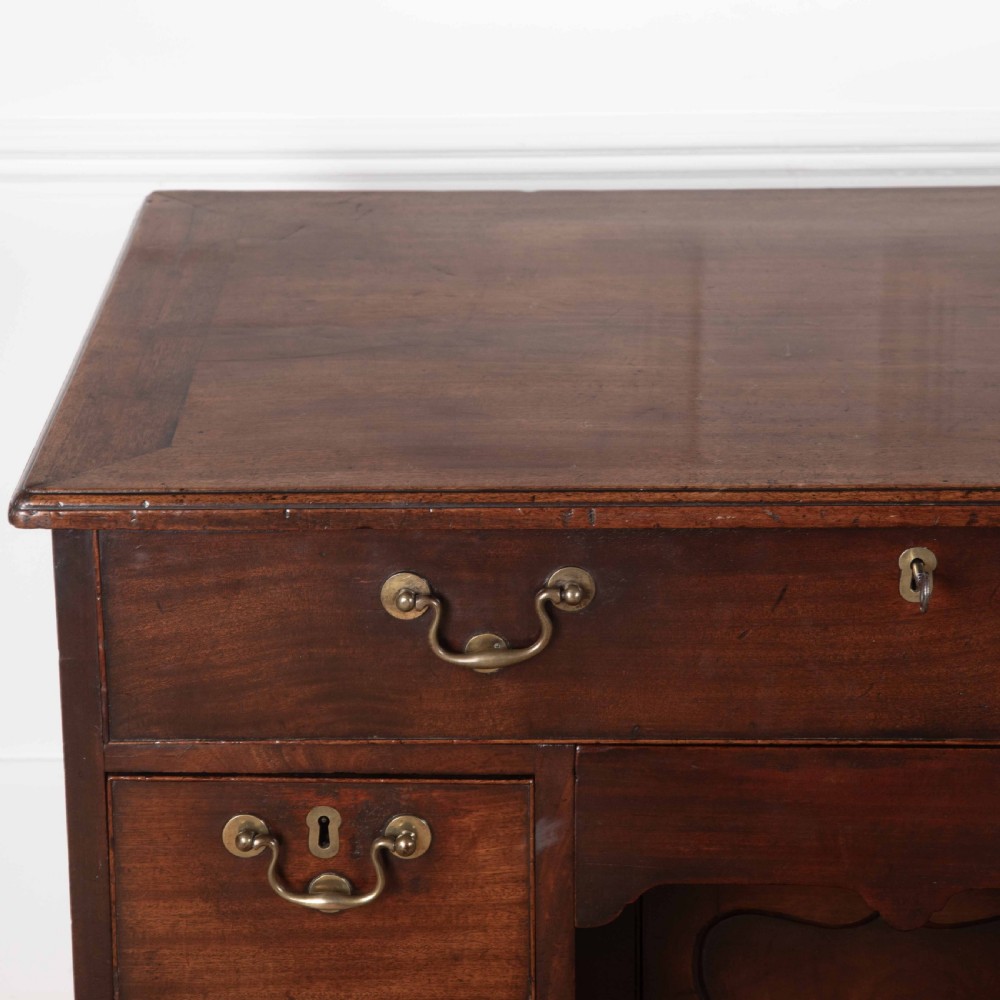 An 18th-century dark mahogany kneehole desk featuring a long top drawer above six side drawers and a central recessed cupboard door with brass handles. View XIV