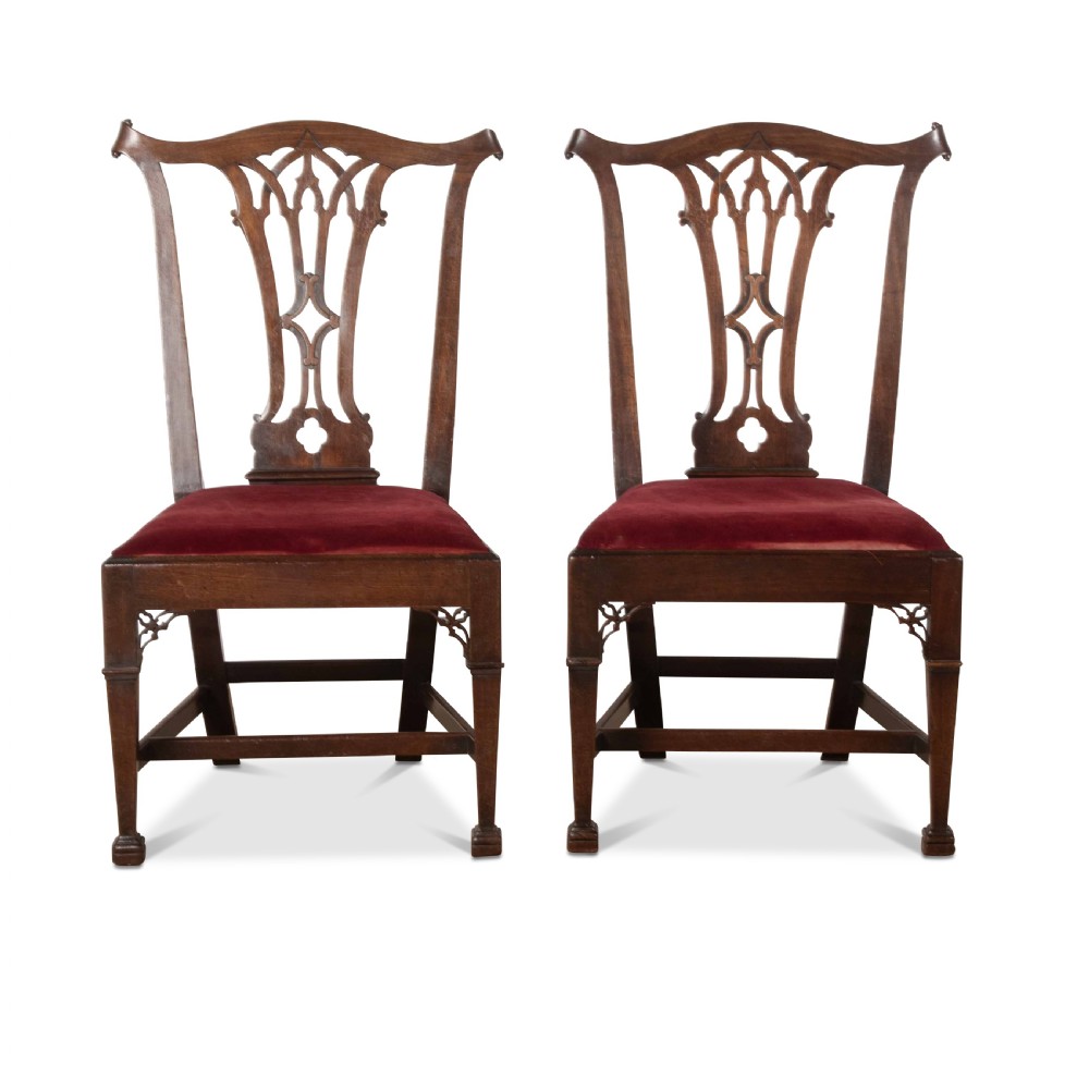 A pair of 18th-century mahogany side chairs featuring pierced Gothic tracery splats and red velvet upholstered seats.