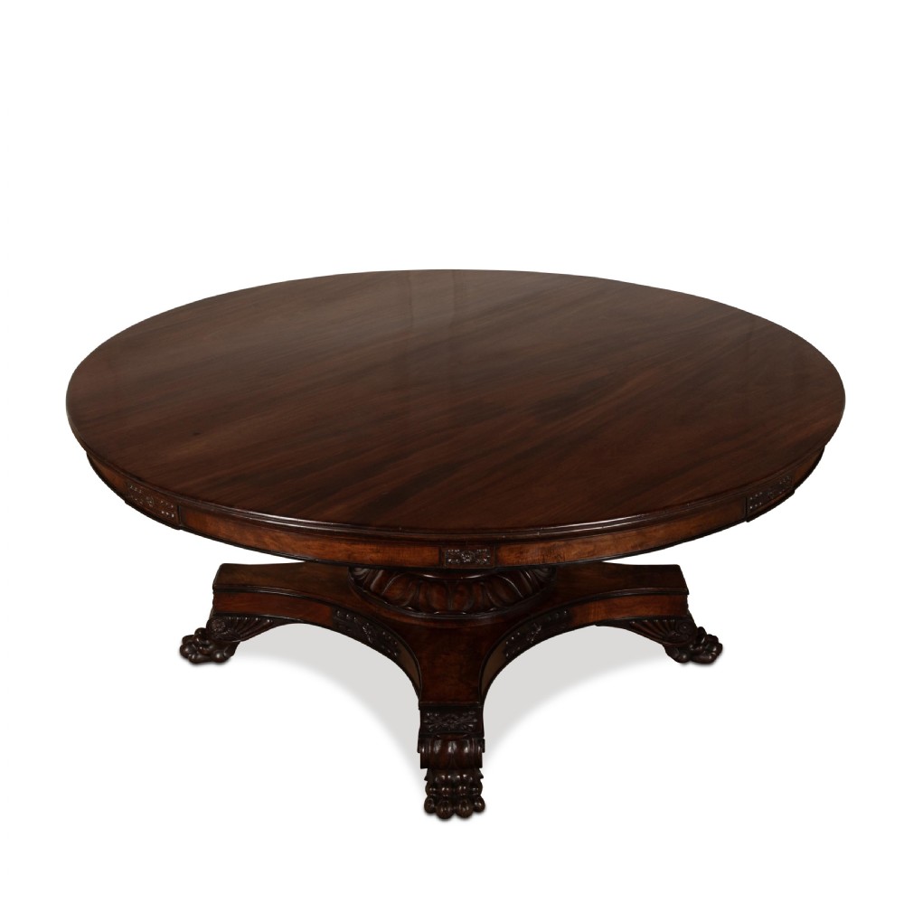 A circular Regency mahogany centre table featuring a carved frieze, a fluted pedestal column, and a concave four-legged plinth base with carved feet. View V