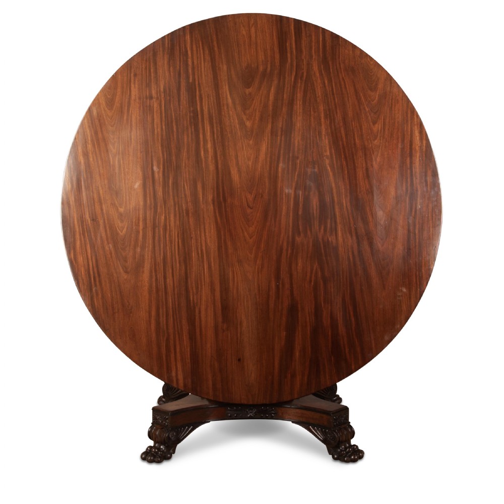 A circular Regency mahogany centre table featuring a carved frieze, a fluted pedestal column, and a concave four-legged plinth base with carved feet. View VI