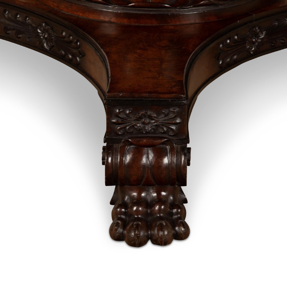 A circular Regency mahogany centre table featuring a carved frieze, a fluted pedestal column, and a concave four-legged plinth base with carved feet. View XII