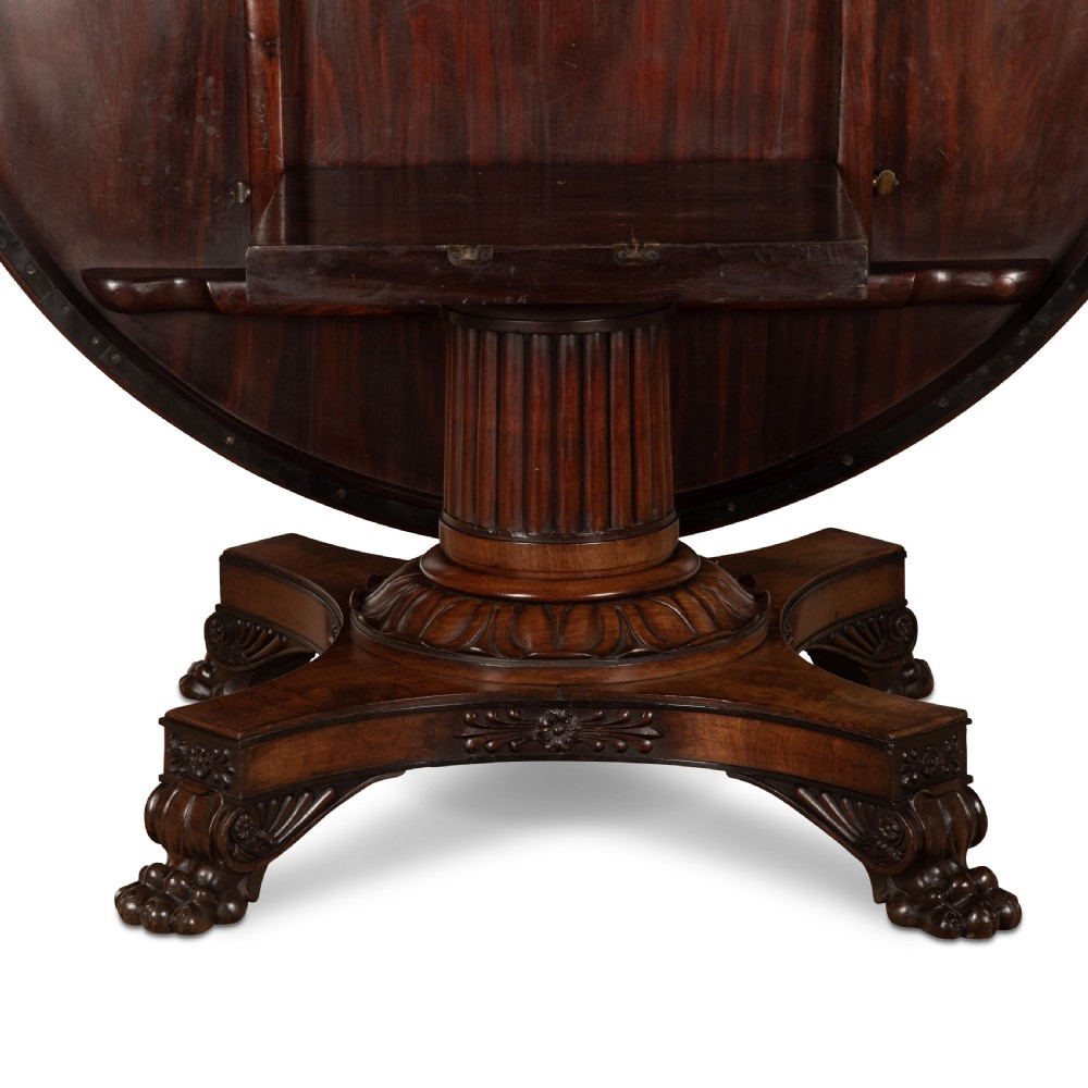 A circular Regency mahogany centre table featuring a carved frieze, a fluted pedestal column, and a concave four-legged plinth base with carved feet. View XIII
