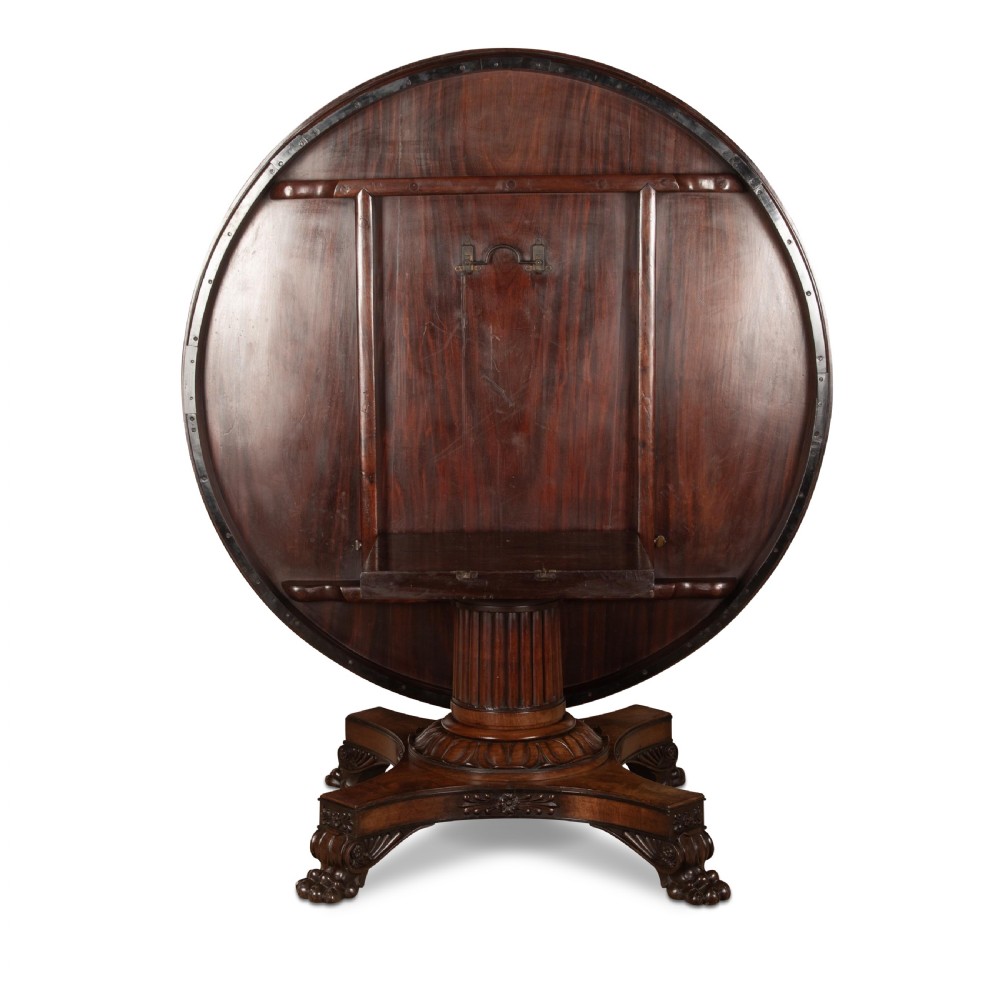 A circular Regency mahogany centre table featuring a carved frieze, a fluted pedestal column, and a concave four-legged plinth base with carved feet. View XIV