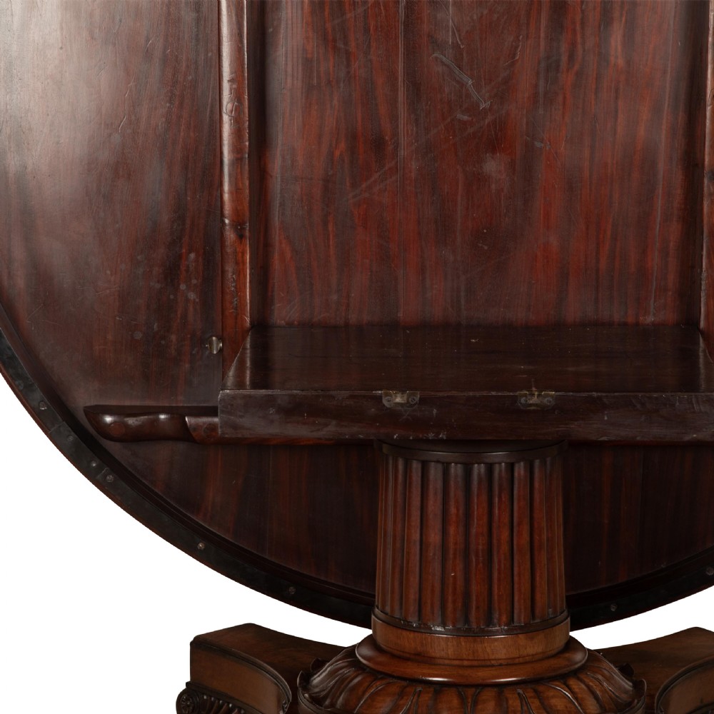 A circular Regency mahogany centre table featuring a carved frieze, a fluted pedestal column, and a concave four-legged plinth base with carved feet. View XV
