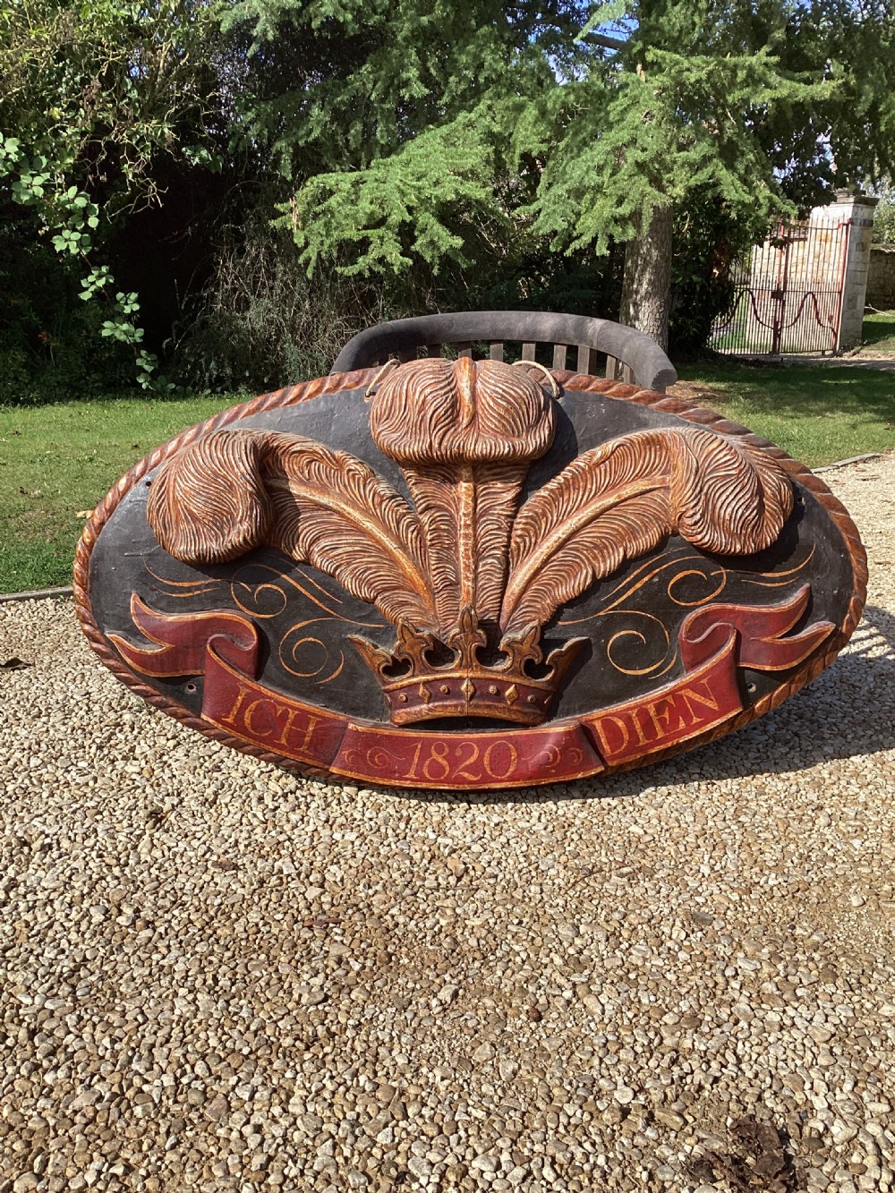 A large oval carved wooden heraldic panel featuring the Prince of Wales ostrich feathers, a crown, and a red banner inscribed with Ich Dien 1820. View III