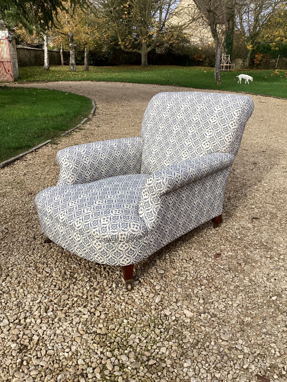 A large Howard and Sons style club armchair upholstered in a blue and white patterned floral fabric with rolled arms and front brass castors.