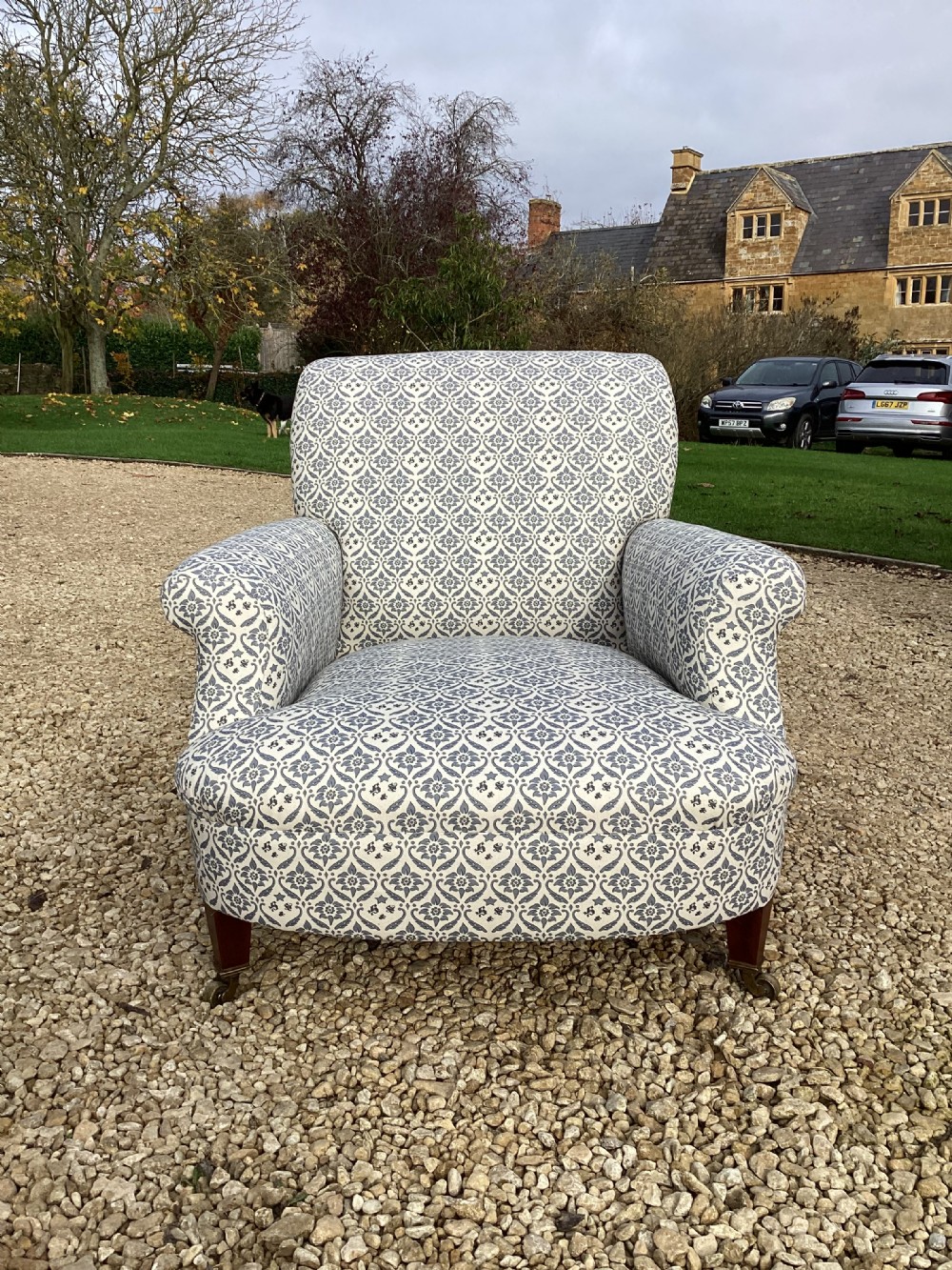 A large Howard and Sons style club armchair upholstered in a blue and white patterned floral fabric with rolled arms and front brass castors. View II