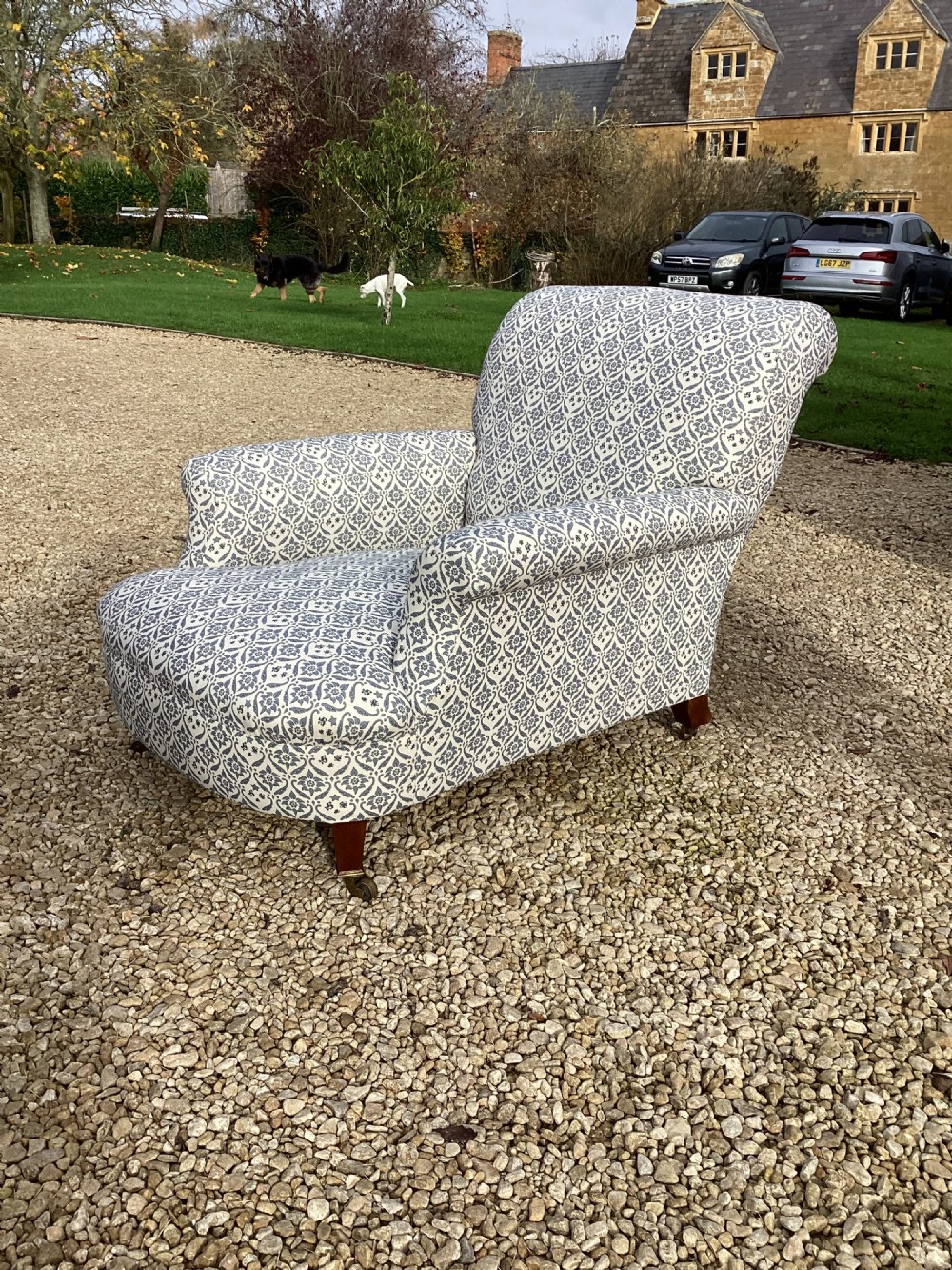 A large Howard and Sons style club armchair upholstered in a blue and white patterned floral fabric with rolled arms and front brass castors. View III