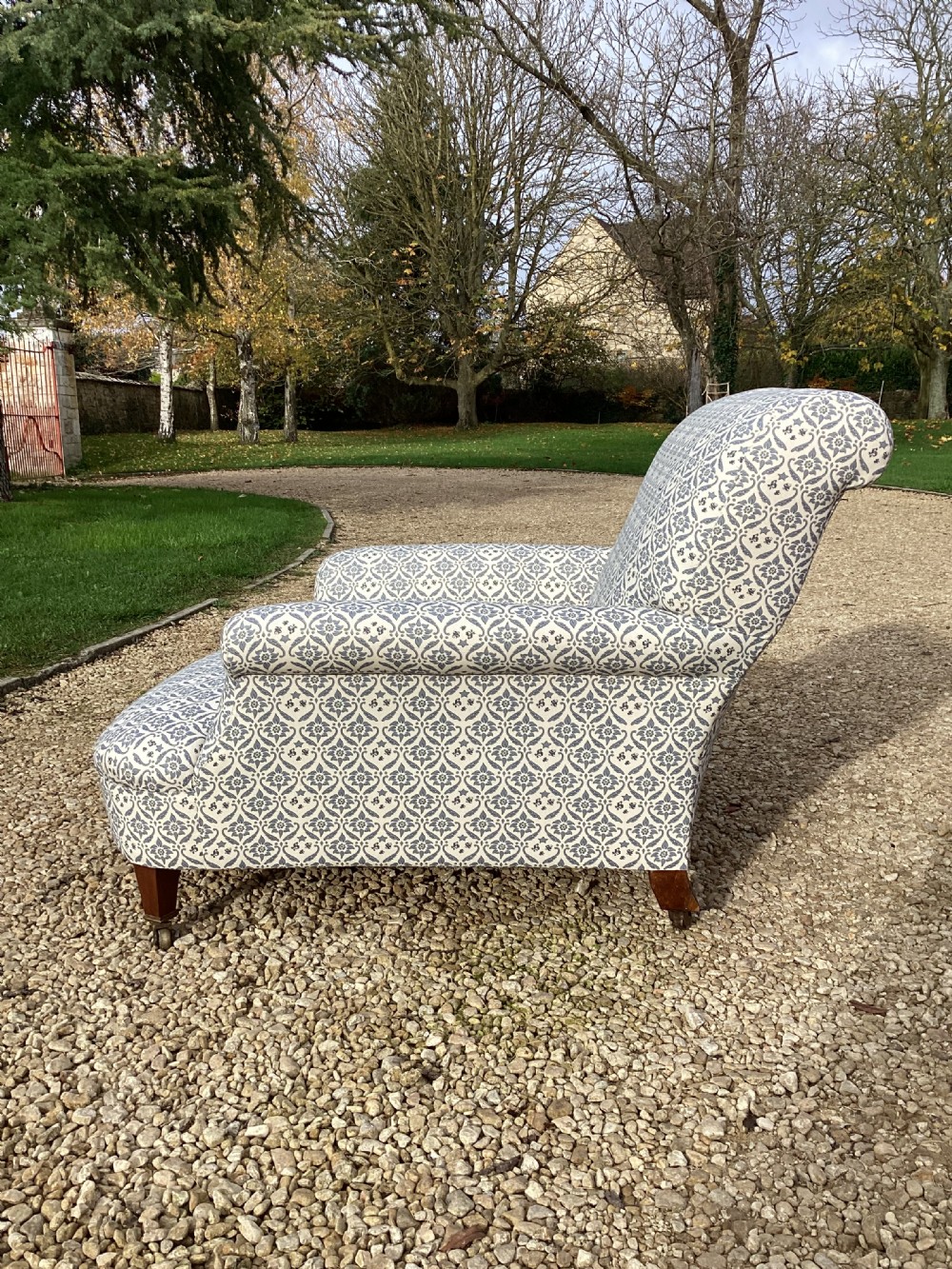 A large Howard and Sons style club armchair upholstered in a blue and white patterned floral fabric with rolled arms and front brass castors. View IV