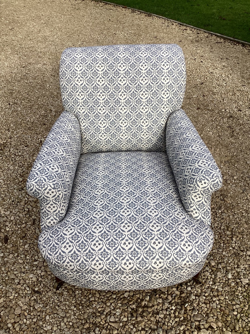A large Howard and Sons style club armchair upholstered in a blue and white patterned floral fabric with rolled arms and front brass castors. View VI